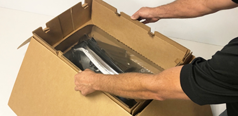 Two arms insert a plastic headlight suspension pack into a custom cardboard box